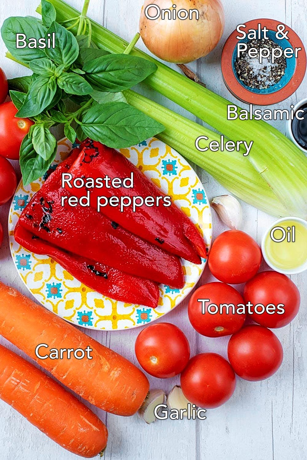 A plate of roasted red peppers surrounded by carrots, tomatoes, celery, basil, garlic and an onion.