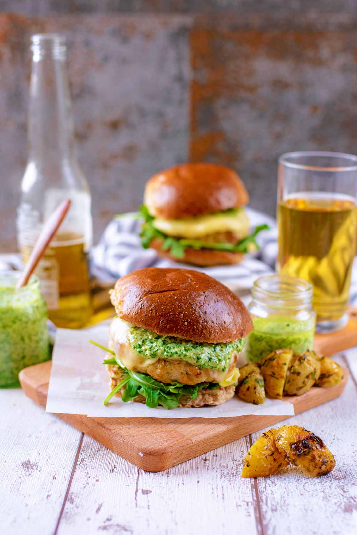 Two chicken burgers with a bottle of beer and jars of pesto.