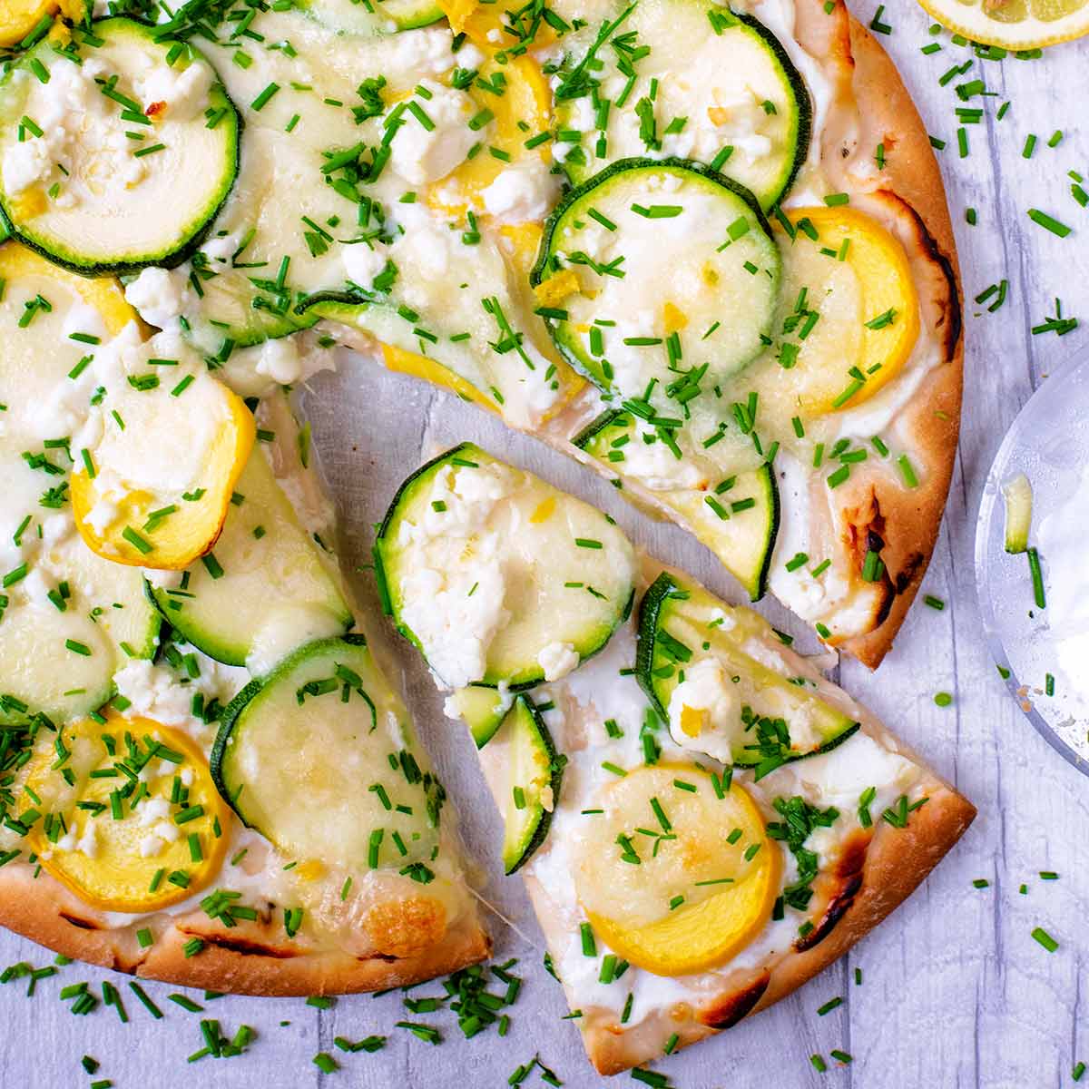 Courgette and lemon pizza on a wooden surface surrounded by sliced courgette.