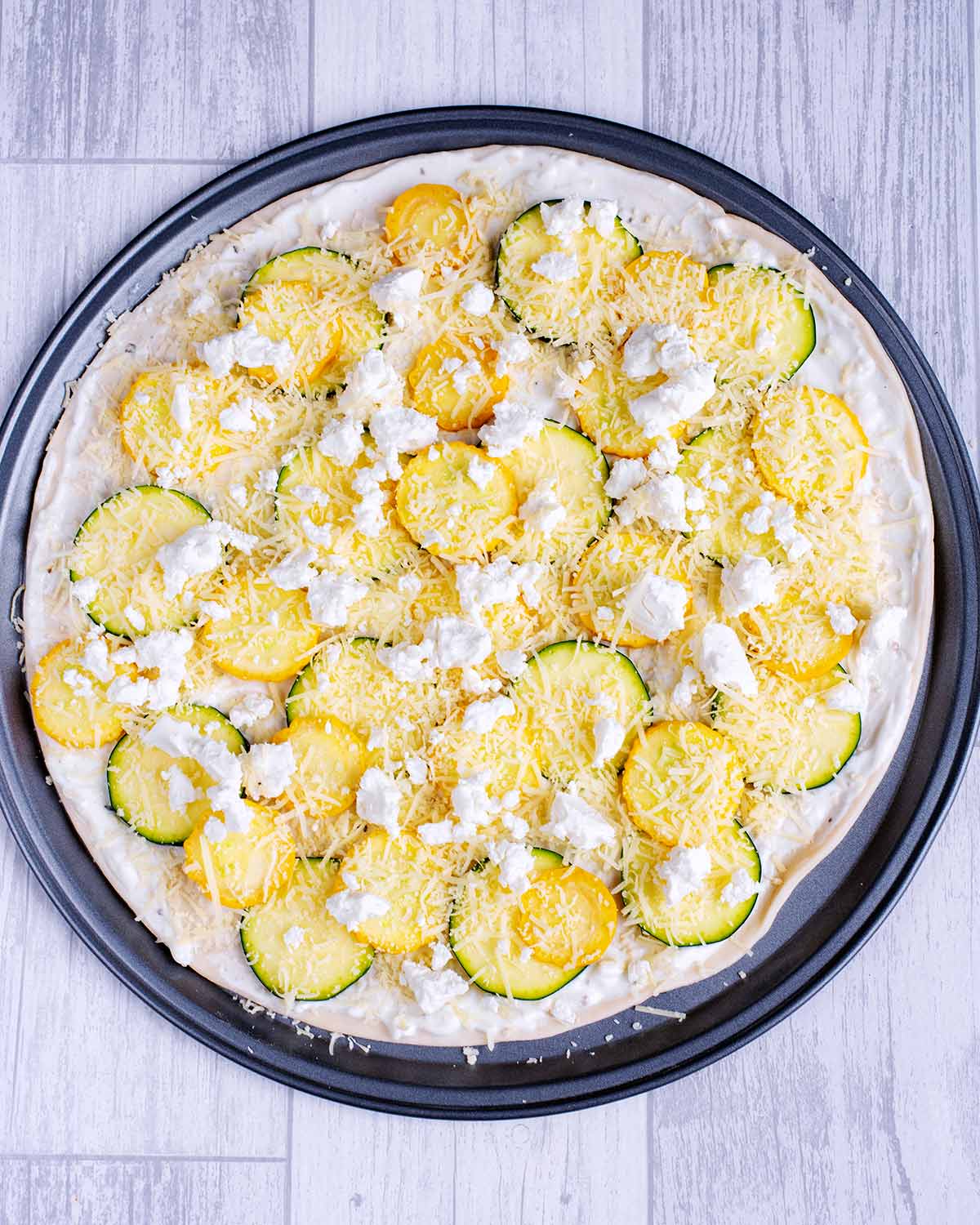 A pizza base topped with a yogurt sauce, sliced courgette and cheese.