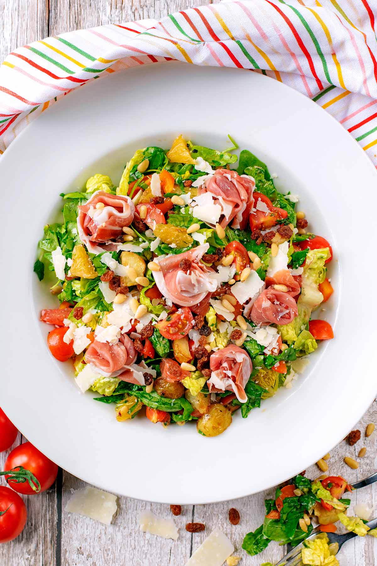 Parma ham sat upon a chopped salad containing leaves, tomatoes, fruit and nuts.