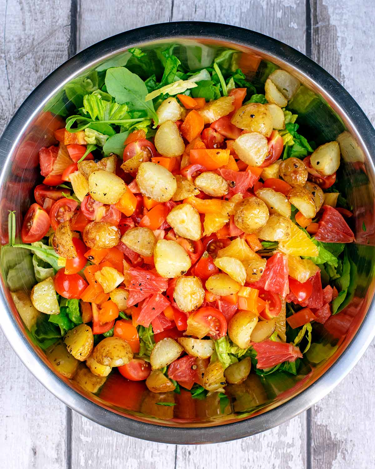 A large mixing bowl containing lettuce, chopped salad vegetables and small roasted potatoes.