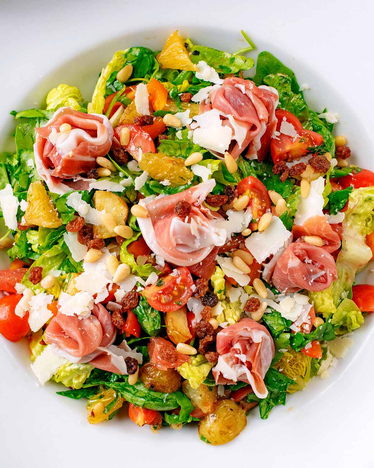 The salad in a serving bowl topped with ham roses and Parmesan shavings.