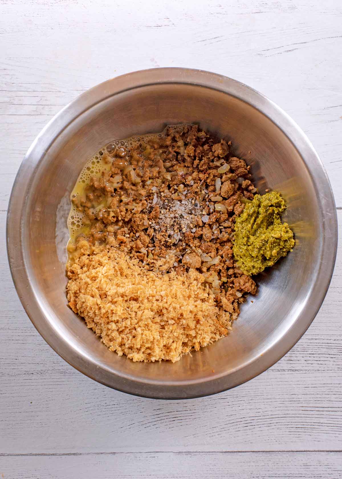 A mixing bowl containing meat free mince, onion, breadcrumbs and pesto.
