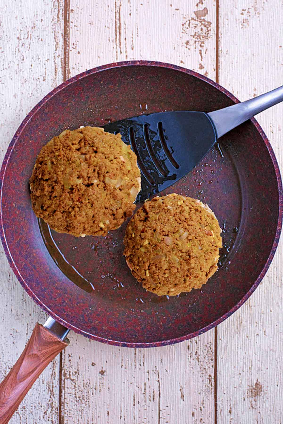 Two meat free quorn burgers cooking in a frying pan. one is about to be flipped.