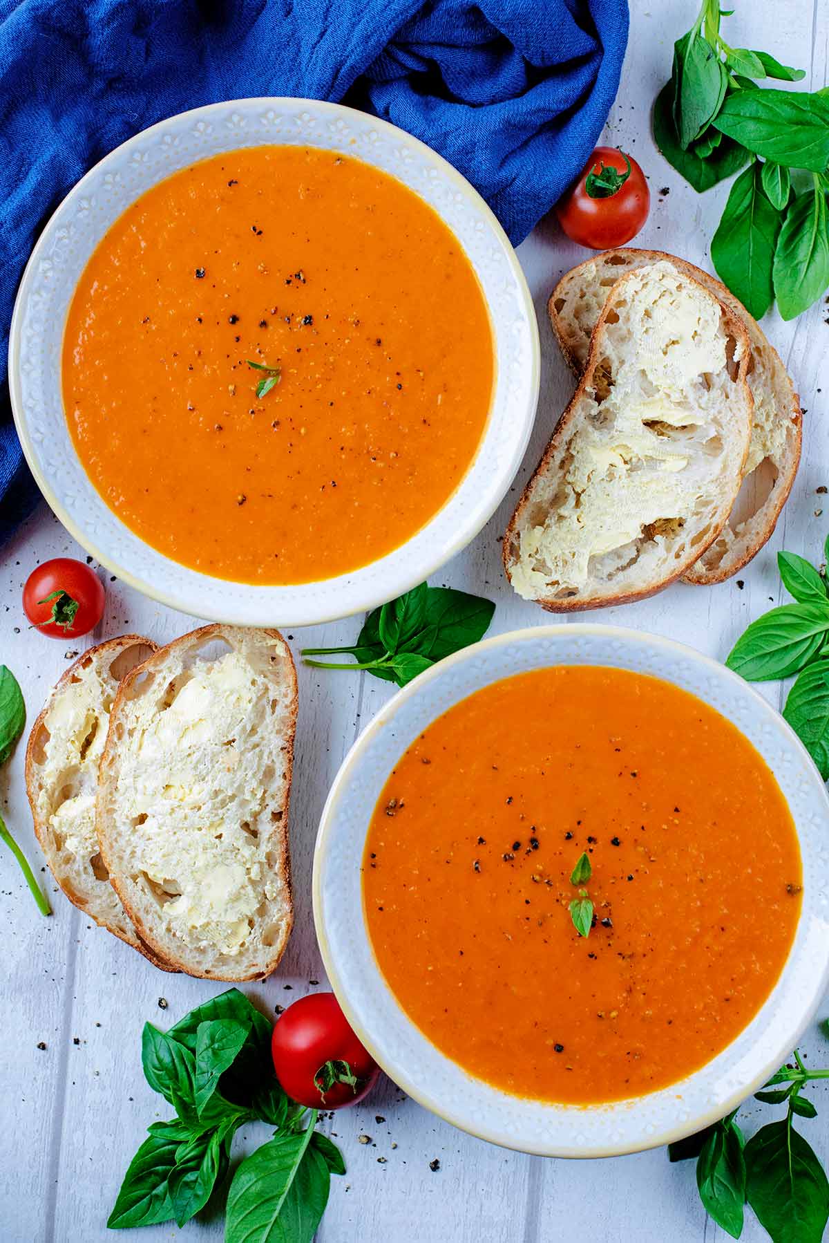 Two bowls of tomato soup with slices of buttered bread and basil leaves.