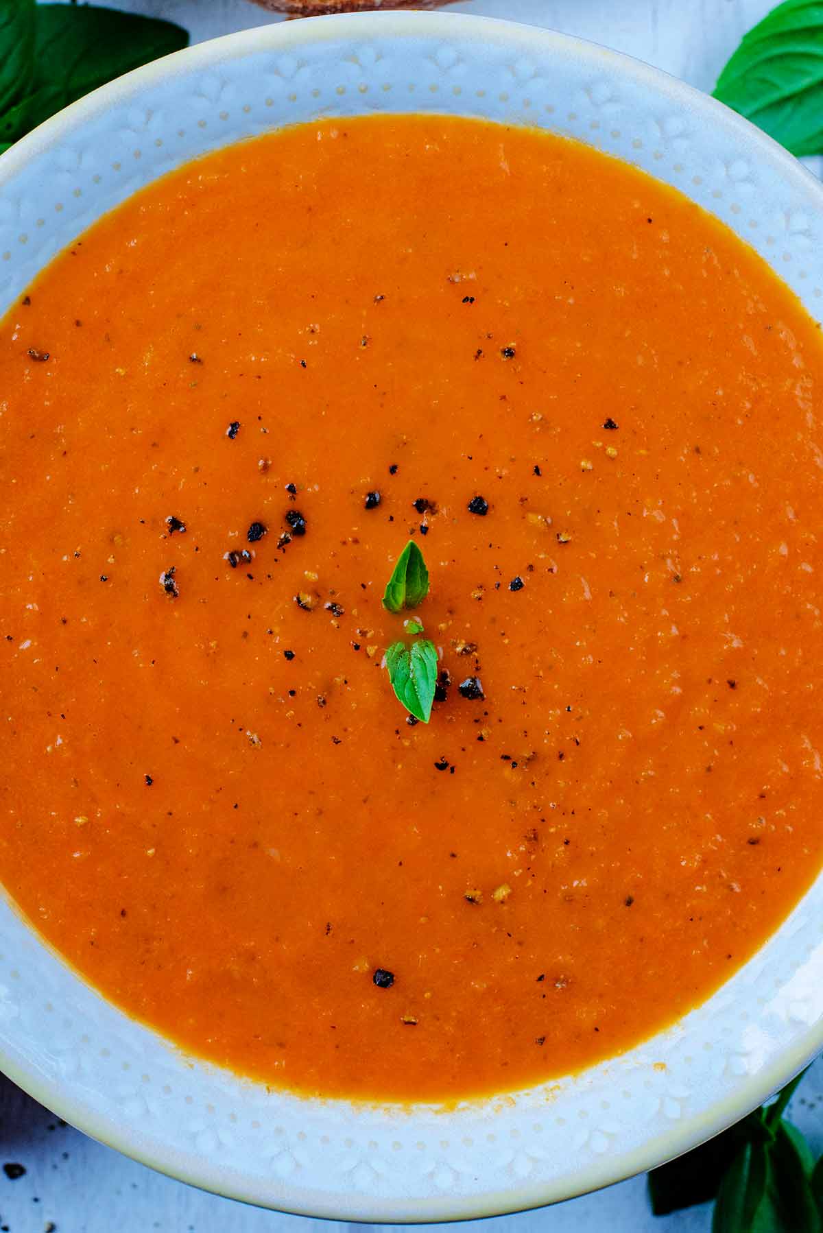 Tomato soup with pepper sprinkled on top and small basil leaves.