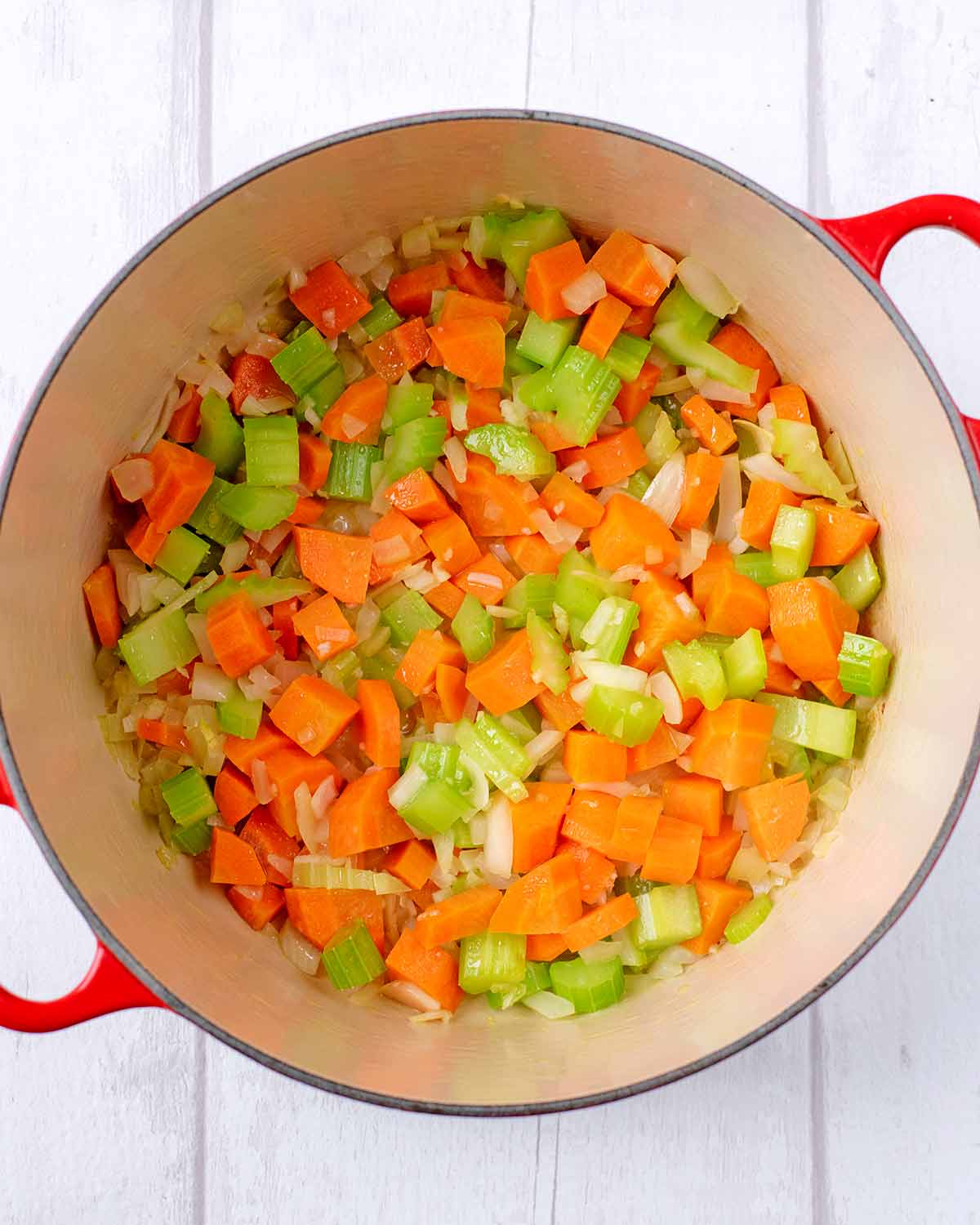 A large red pan with chopped celery and carrot.