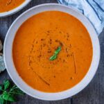 A bowl of Roasted Red Pepper and Tomato Soup with small basil leaves on top.