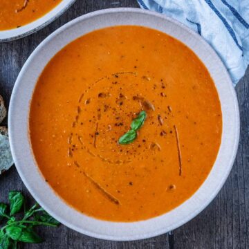 A bowl of Roasted Red Pepper and Tomato Soup with small basil leaves on top.