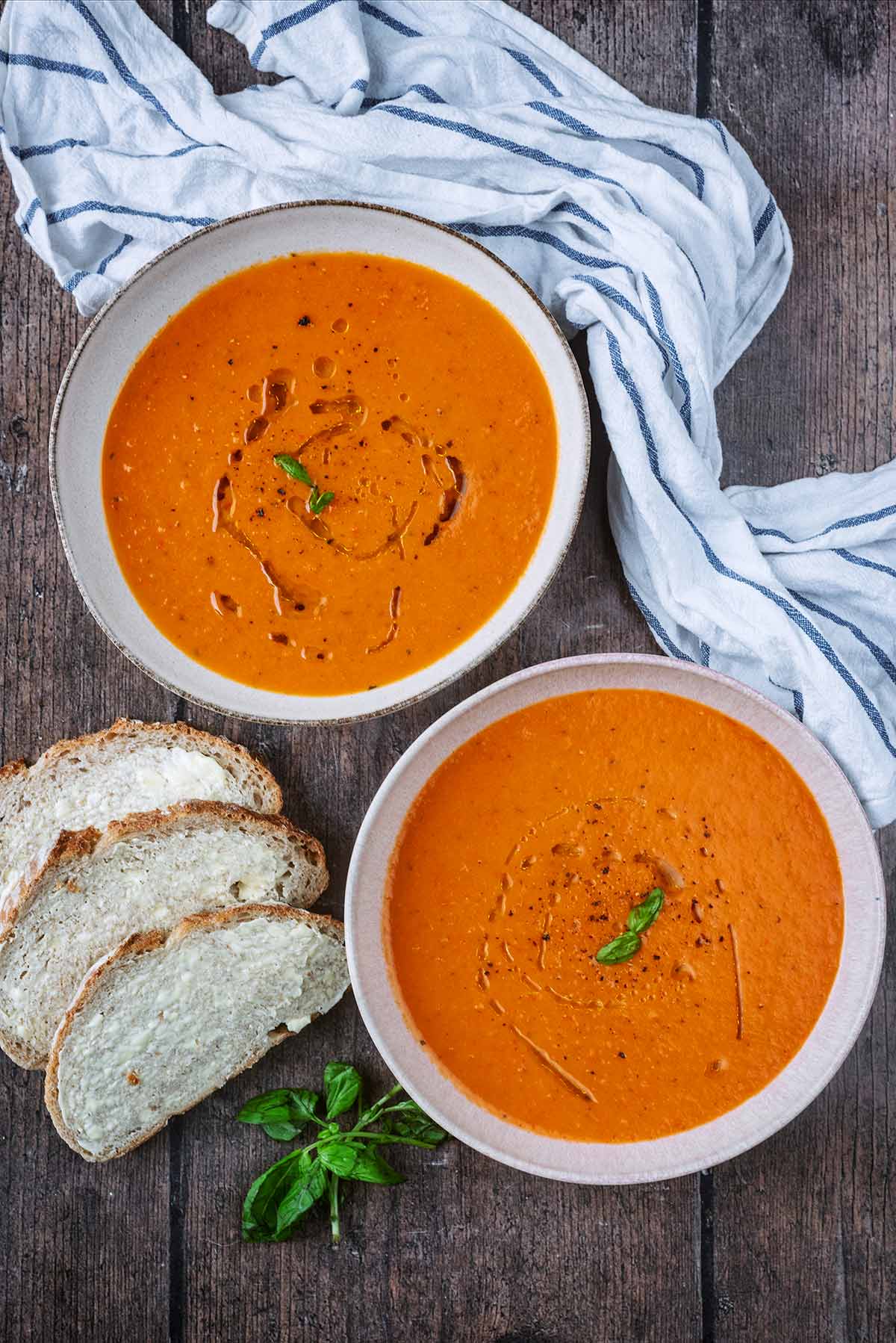 Two bowls of red pepper and tomato soup with three slices of buttered bread.