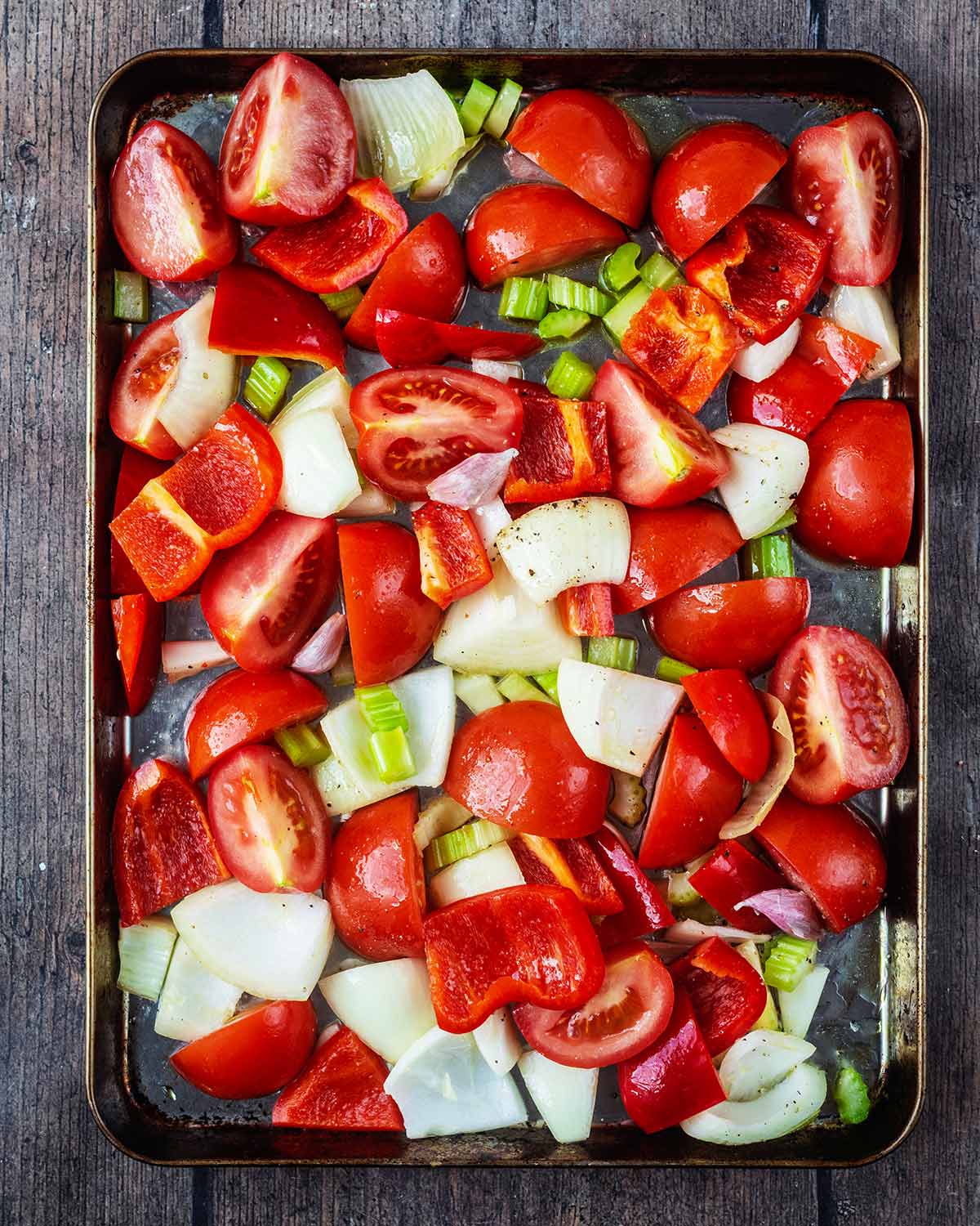 Chopped tomatoes, onions, celery and bell pepper on a baking tray.