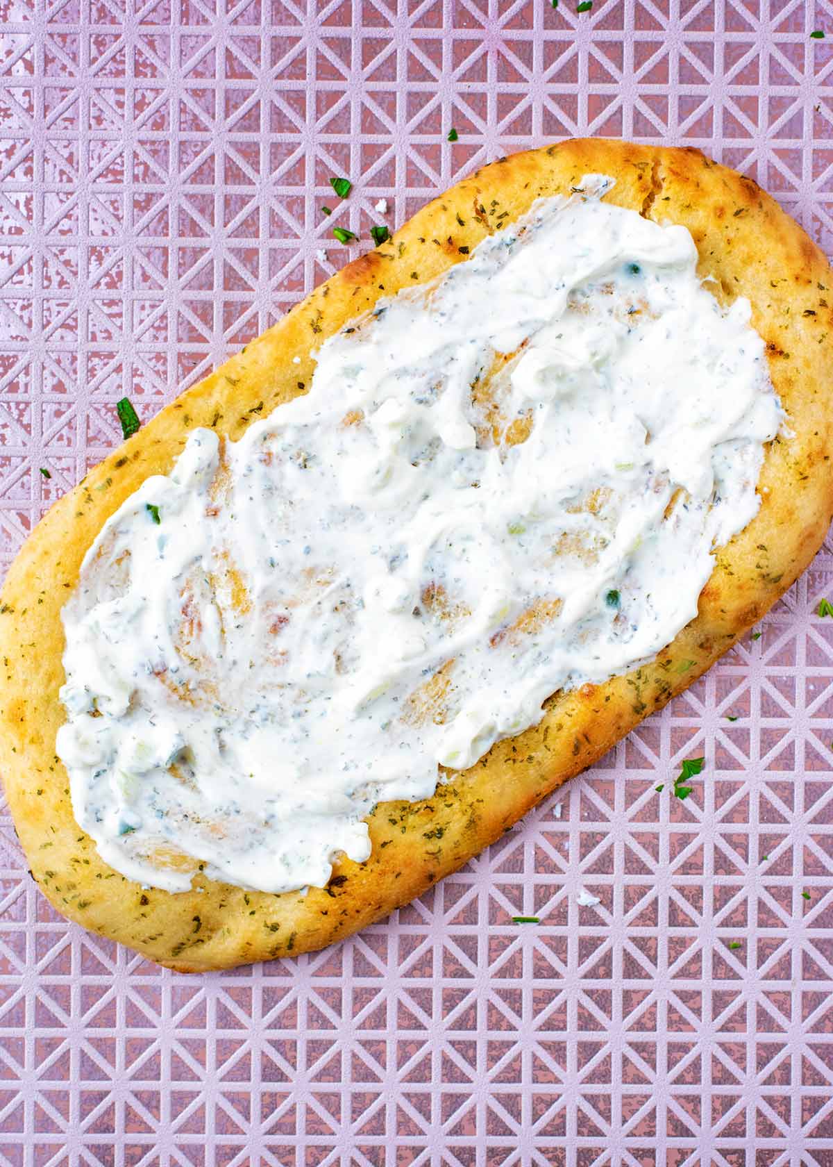 A flatbread with tzatziki spread over it.