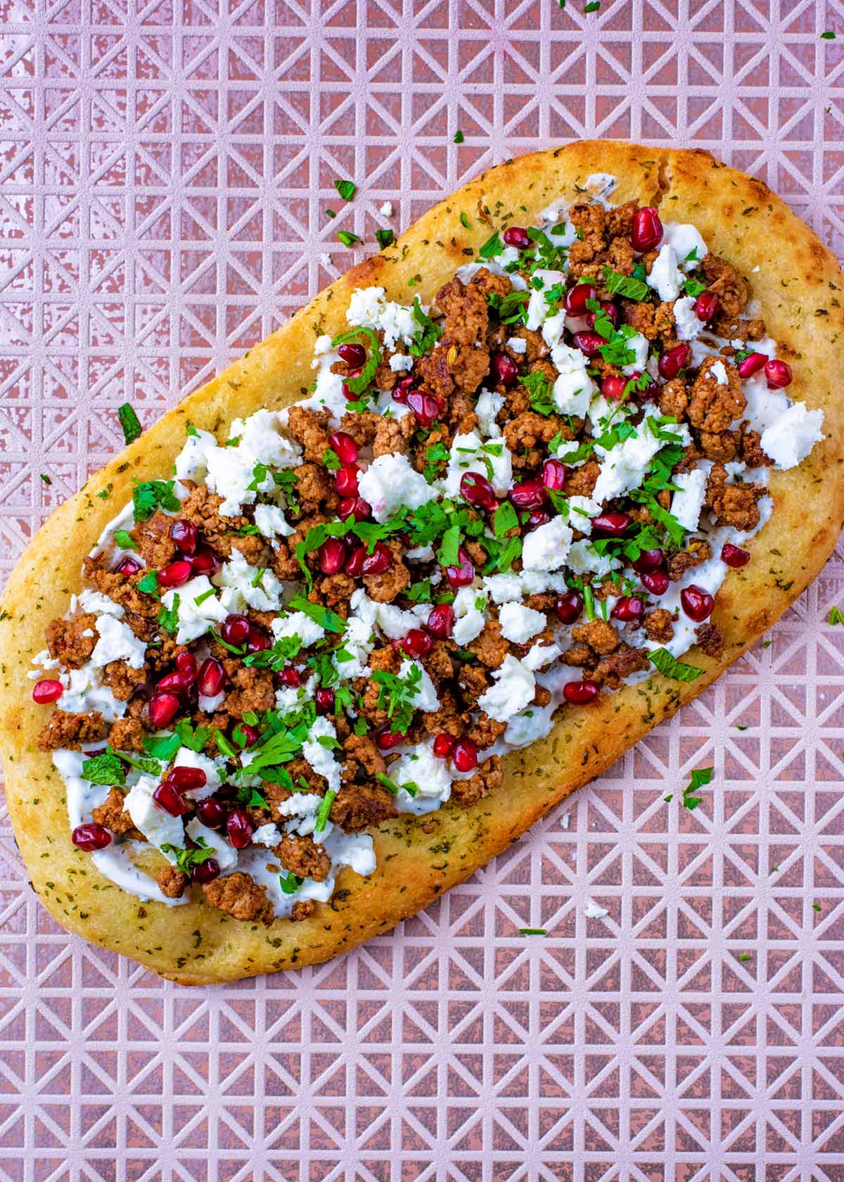 A flatbread topped with tzatziki, lamb, feta cheese, pomegranate seeds and herbs.