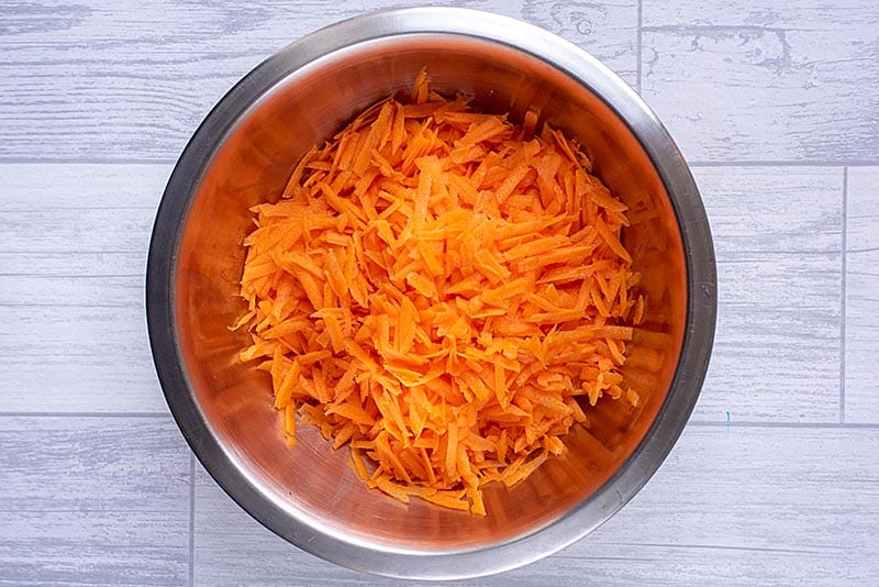 A large metal bowl full of grated carrot.