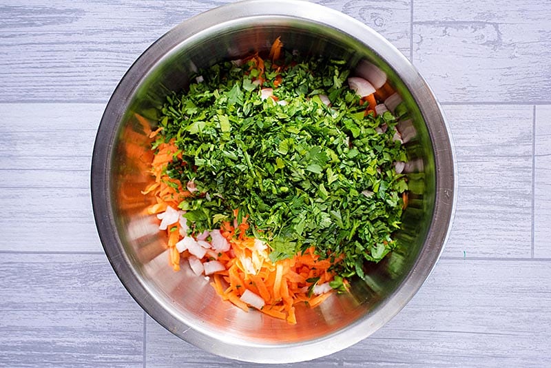 A large metal bowl full of grated carrot, chopped onion and cilantro.