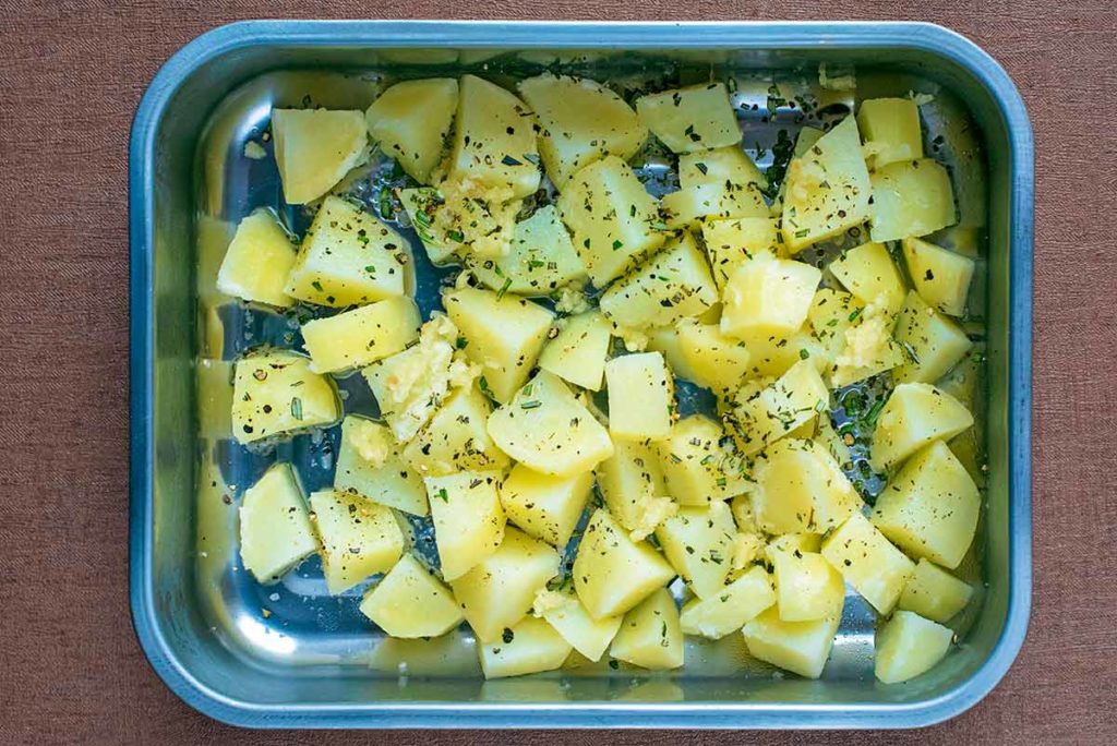 A roasting tin with the par-boiled potatoes and herbs in it.