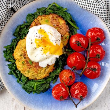 A poached egg, yolk running out, on top of two oven baked baked hash browns. Roasted tomatoes next to them