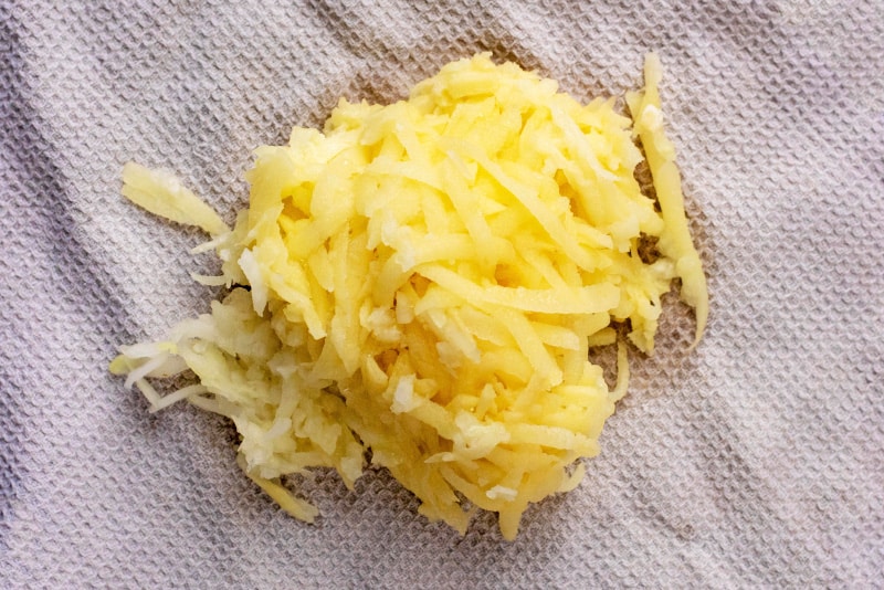 A pile of grated potato and onion on a white kitchen towel.