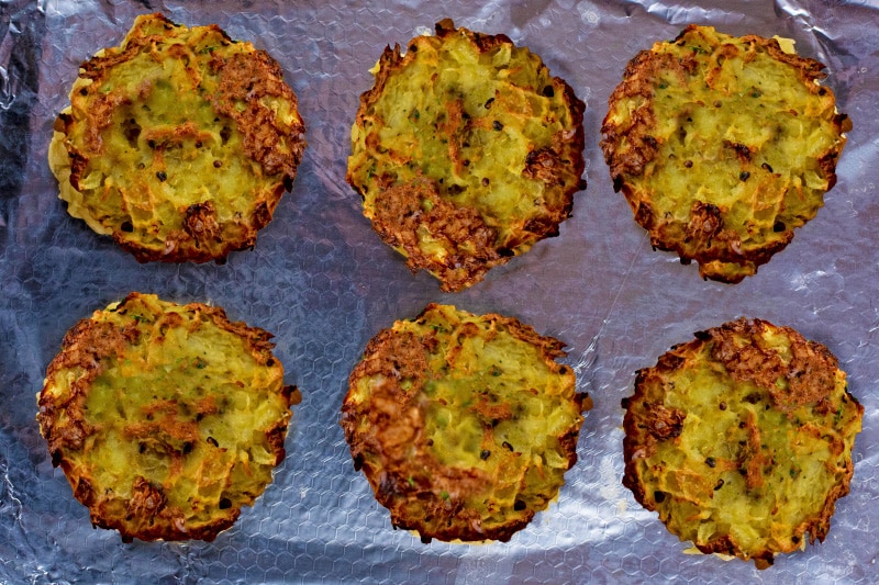 Six cooked hash brown patties on a metal baking tray.