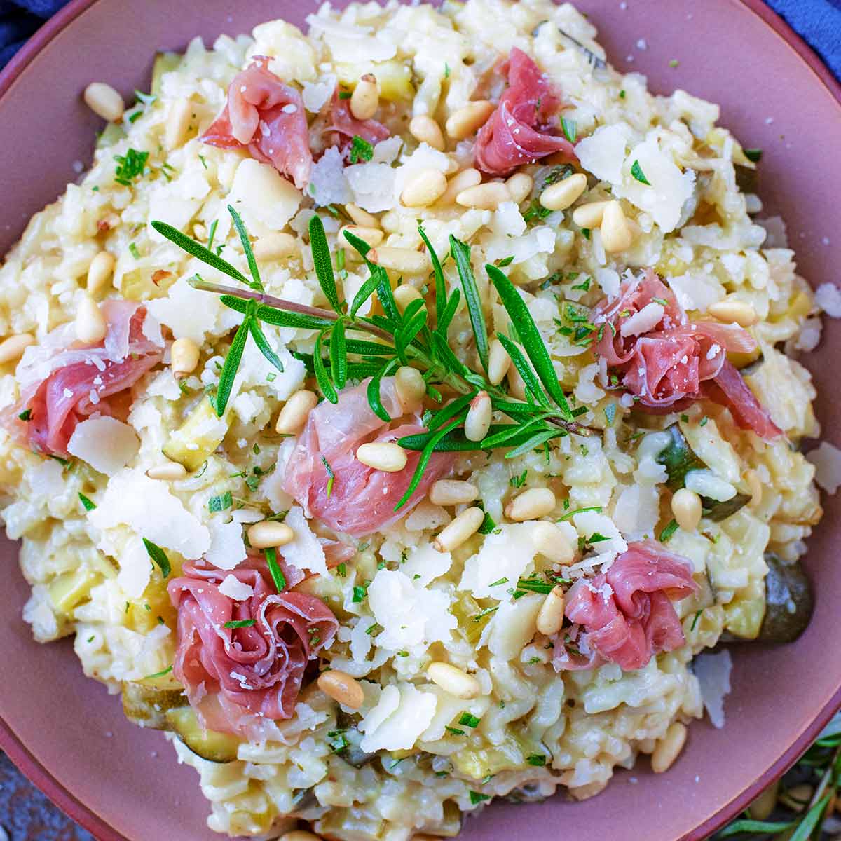 Courgette Risotto in a pink bowl with rosemary sprig on top.