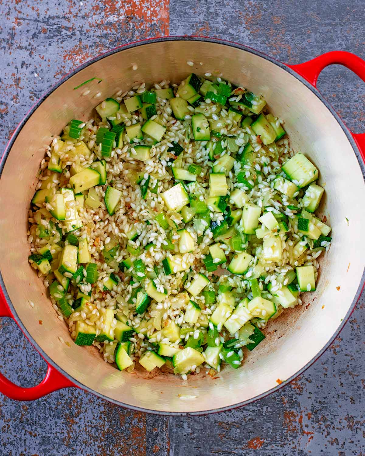 A large red pan with celery, shallots, courgette and risotto rice.