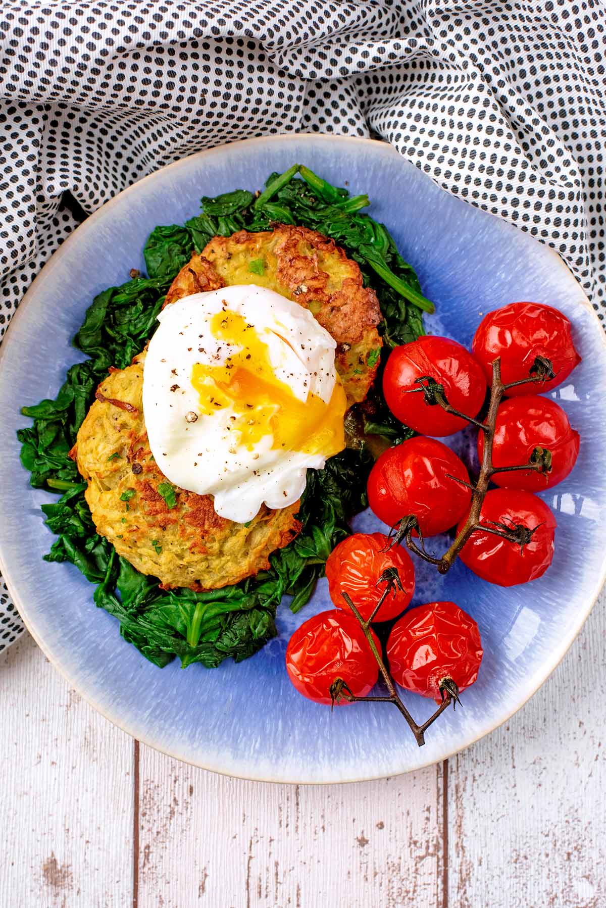 A poached egg on top of two hash browns next to some cooked tomatoes.