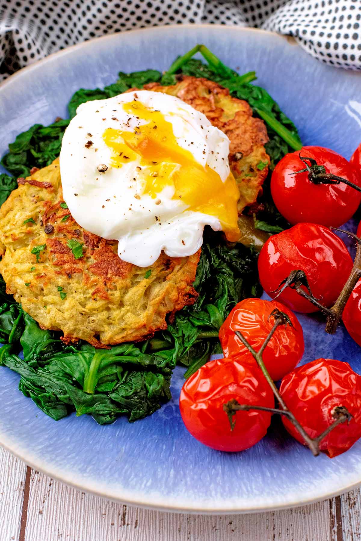 Hash Browns with a poached egg, spinach and cherry tomatoes, all on a blue plate.