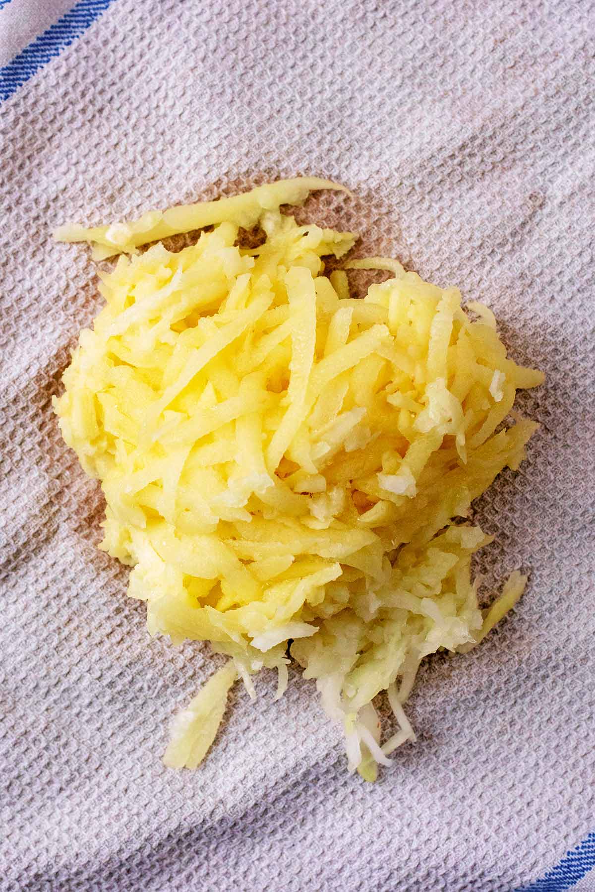 A pile of grated potato and onion on a white kitchen towel.