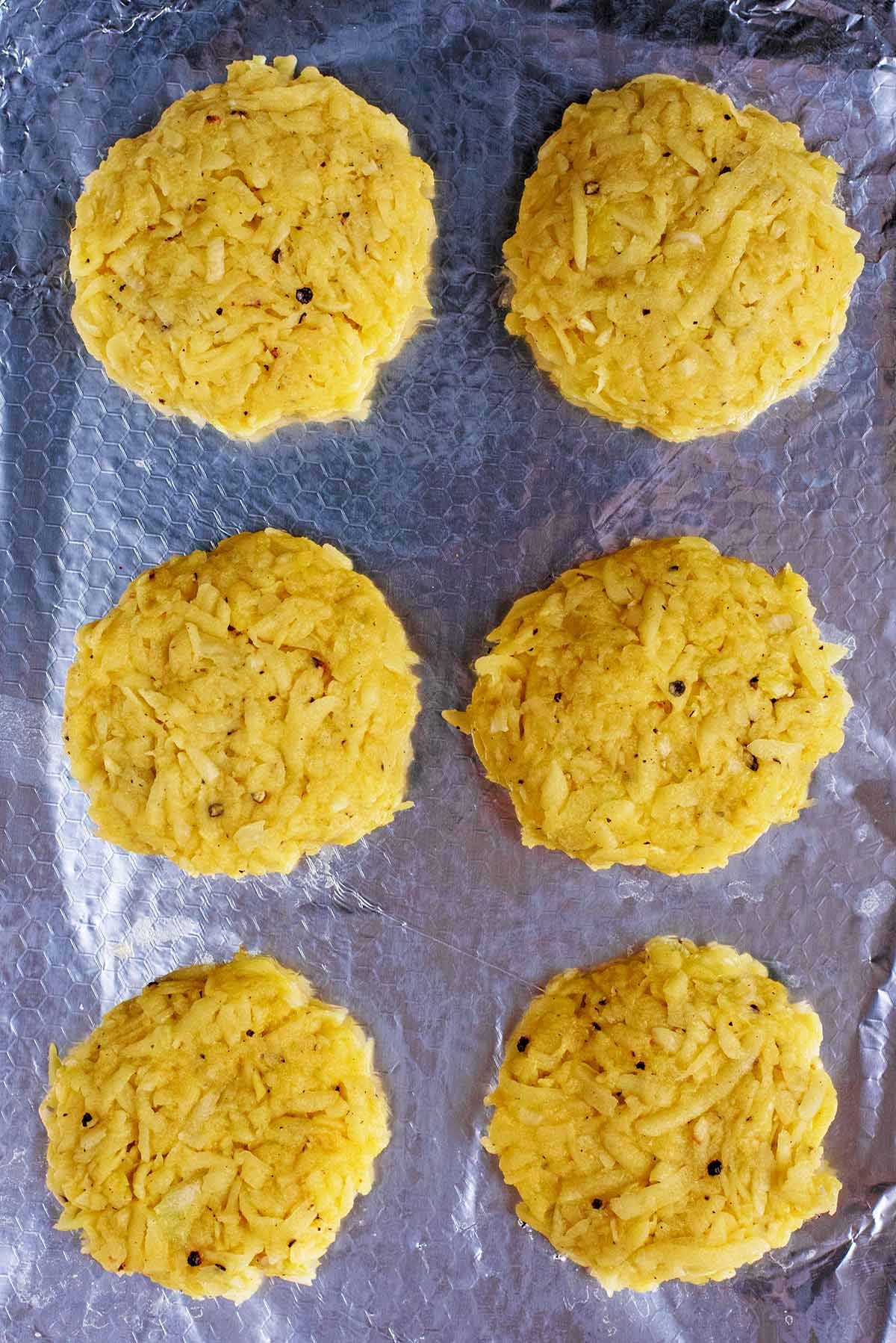 Six hash brown patties on a metal baking tray.