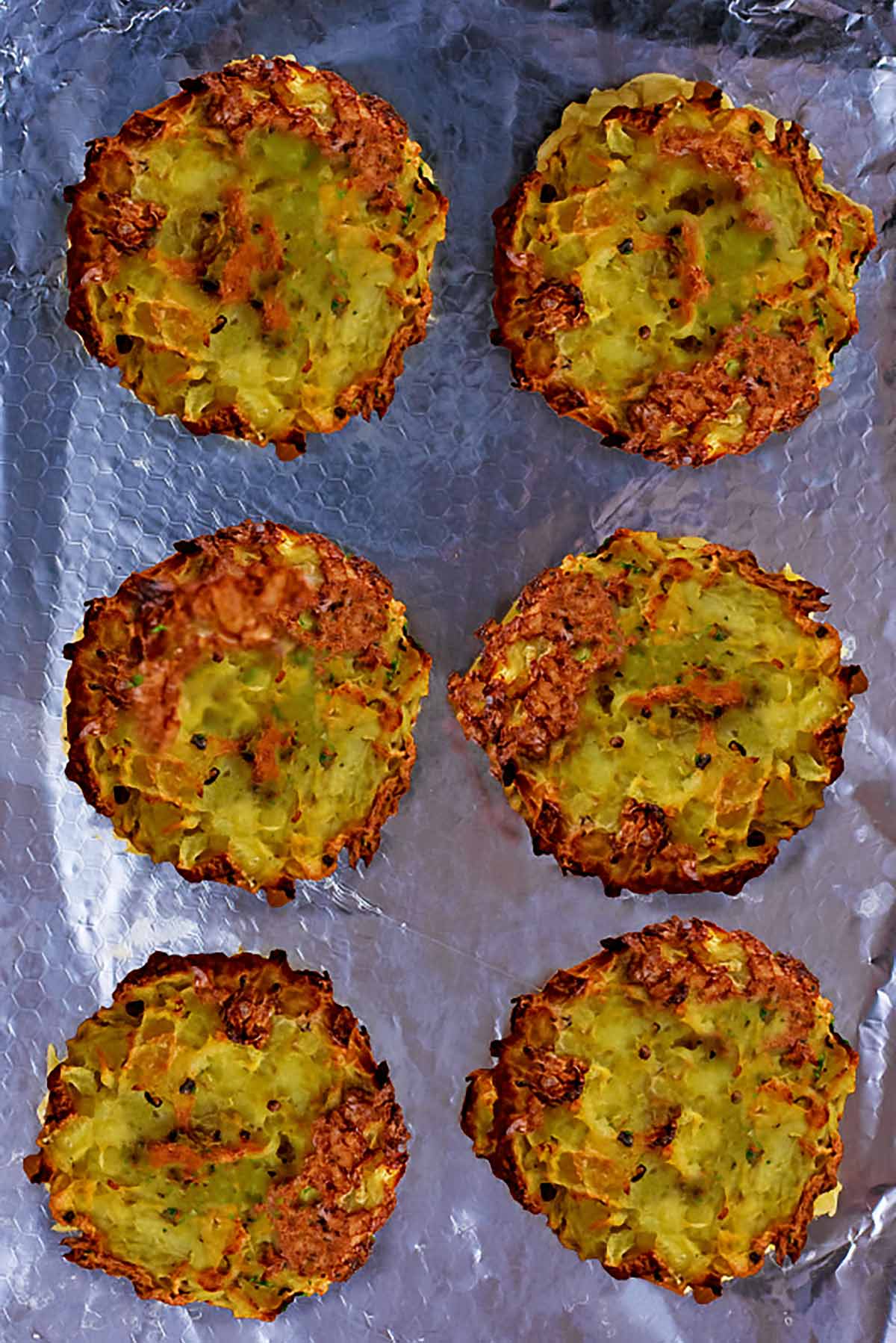 Six cooked hash brown patties on a metal baking tray.