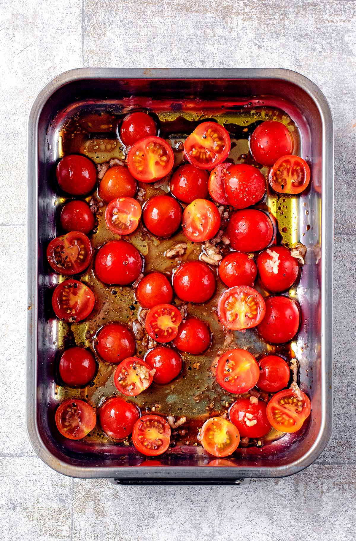 Halved cherry tomatoes roasting in a pan.
