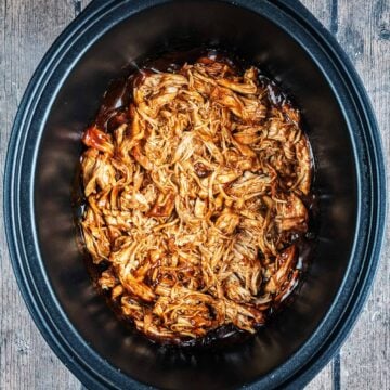 Slow cooker BBQ chicken in a black slow cooker bowl.