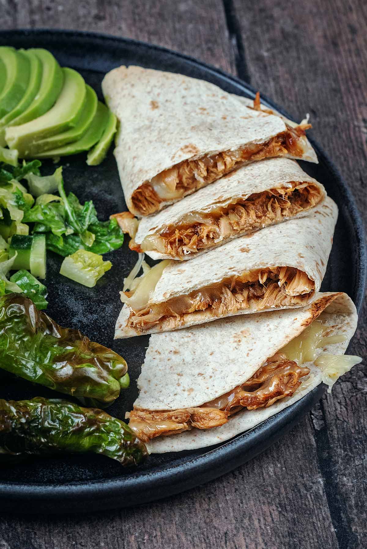 BBQ chicken quesadillas on a plate with avocado, salad and peppers.
