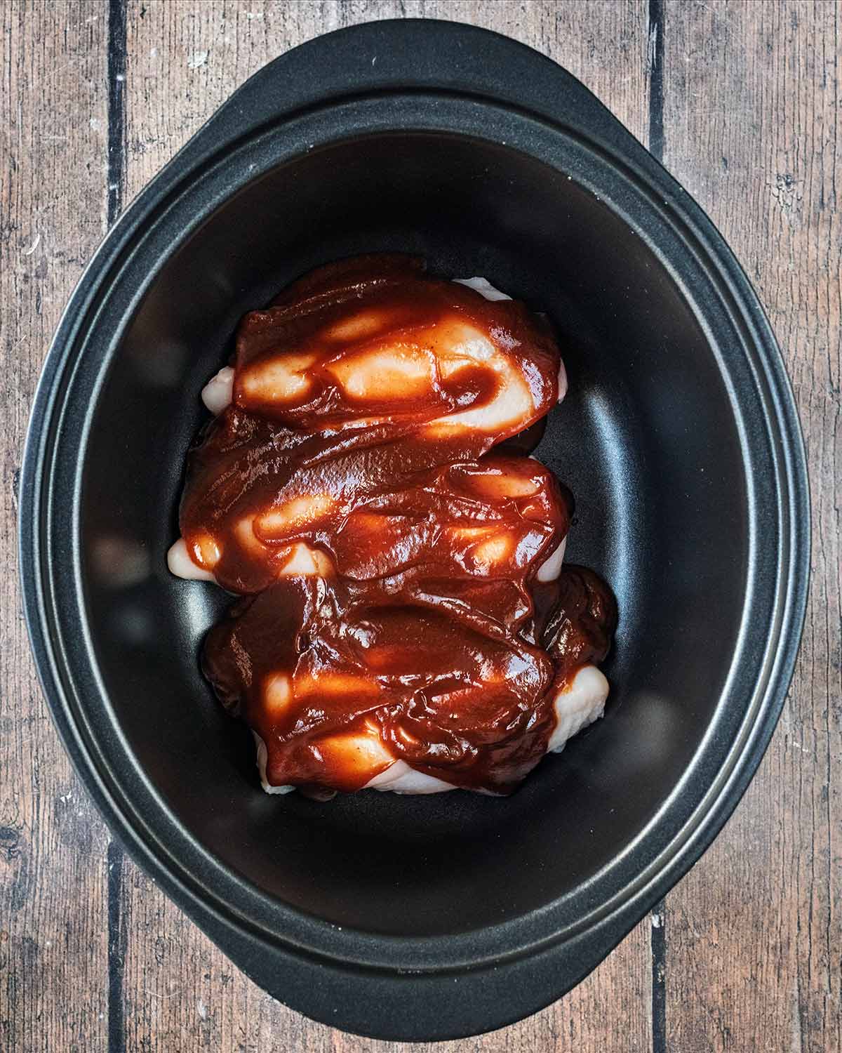 Chicken breasts in a slow cooker bowl covered in barbecue sauce.