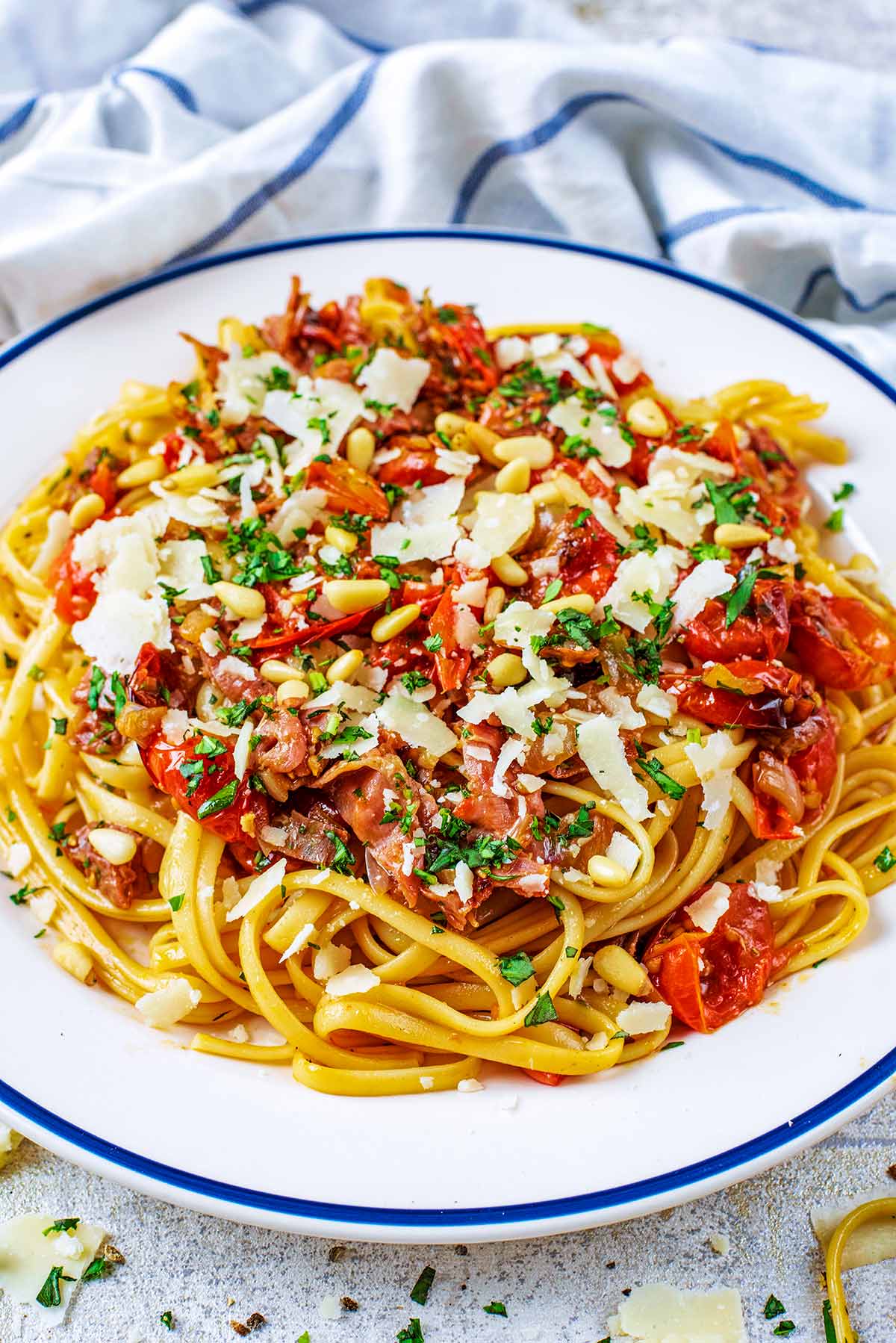 A tomato pasta dish with ham, basil and parmesan, all on a white plate in front of a striped towel.