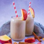 Two glasses of apple pie smoothie with apple slices.