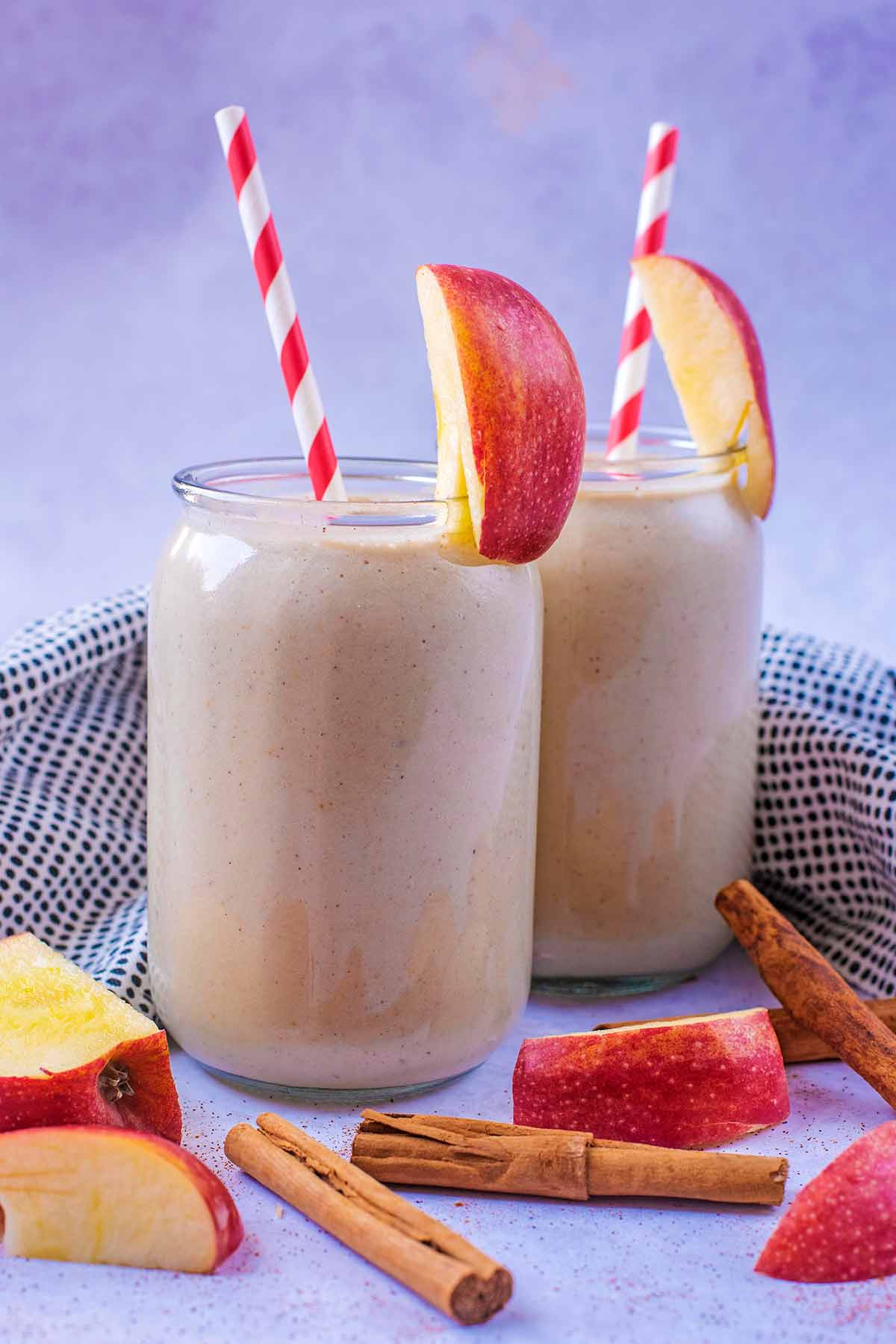 Two jars of smoothie with apple wedges on the rims.