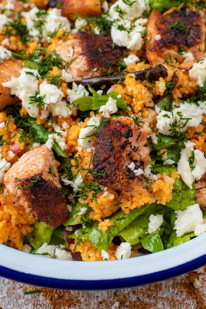 Grilled salmon pieces and feta cheese on top of salad leaves.