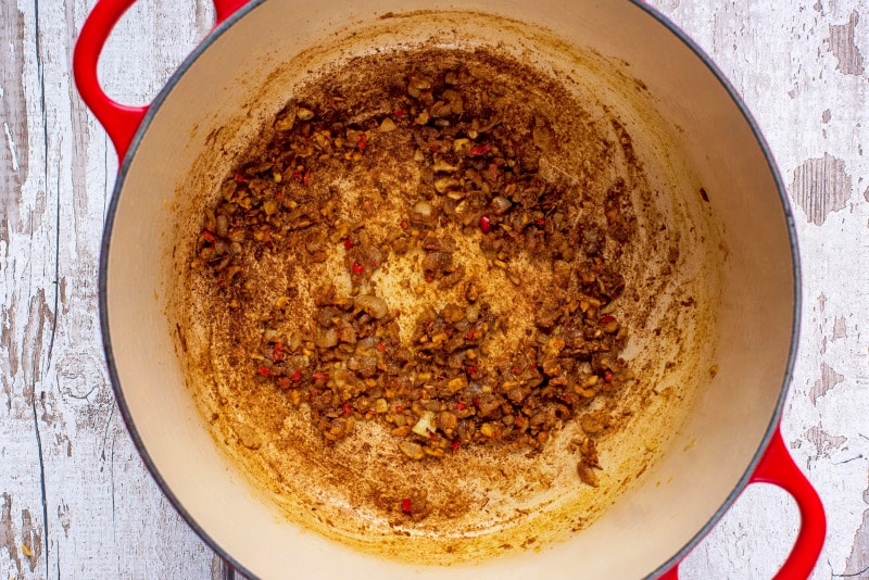 A large red pan with cooked shallots, chili, garlic, ginger and curry powder.