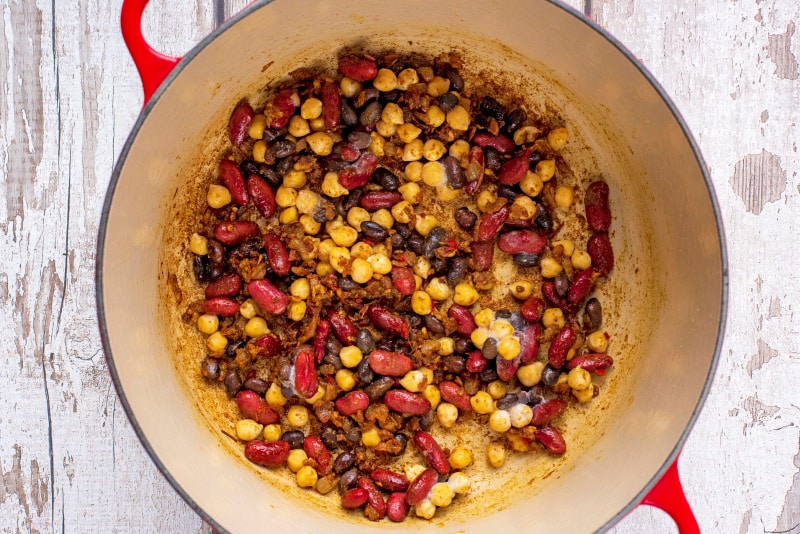 A large red pan with cooked shallots, chili, garlic, ginger, curry powder and mixed beans.