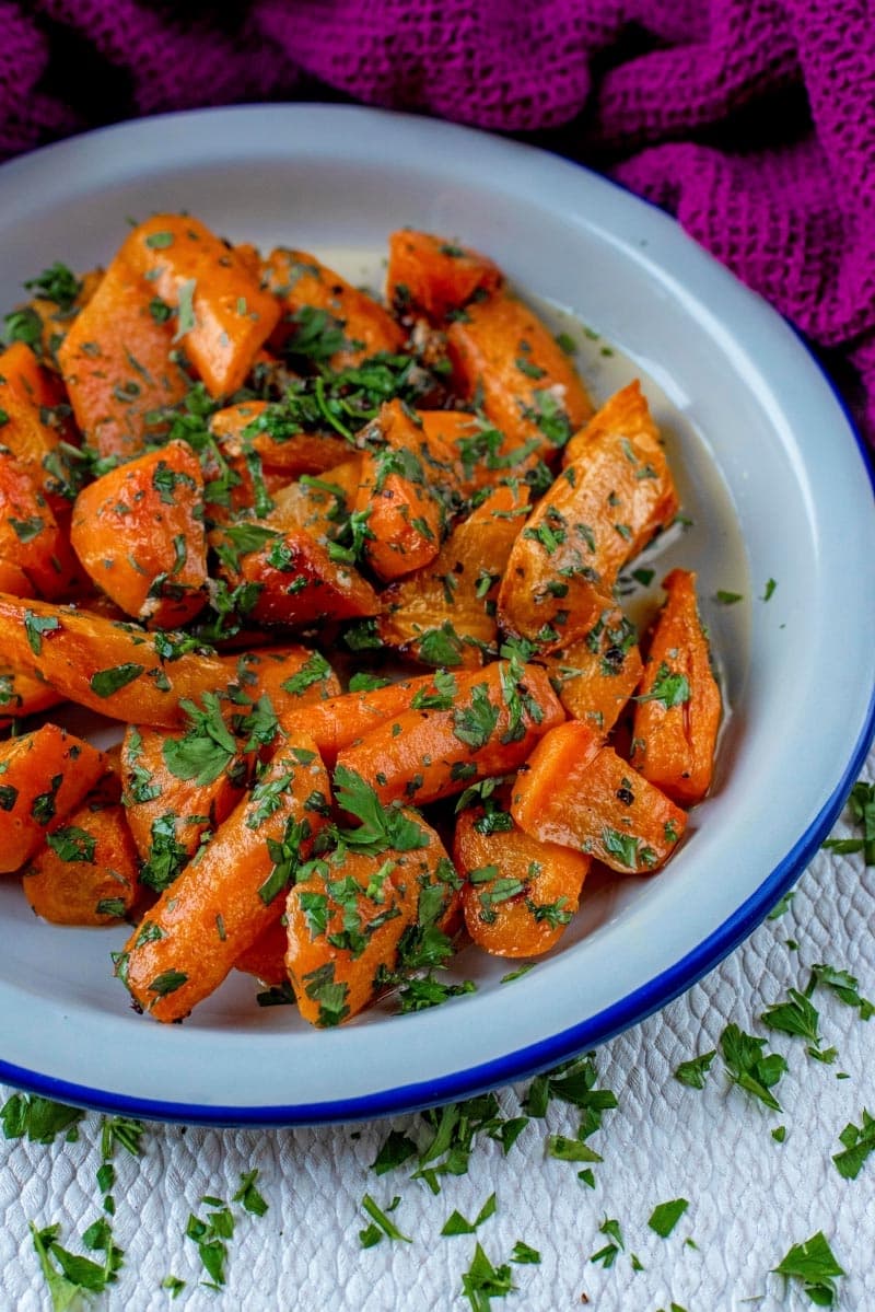 Carrots and herbs in a blue rimmed white bowl.