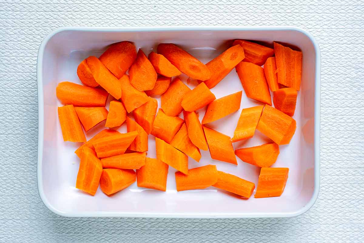 A white baking dish containing chopped raw carrots.