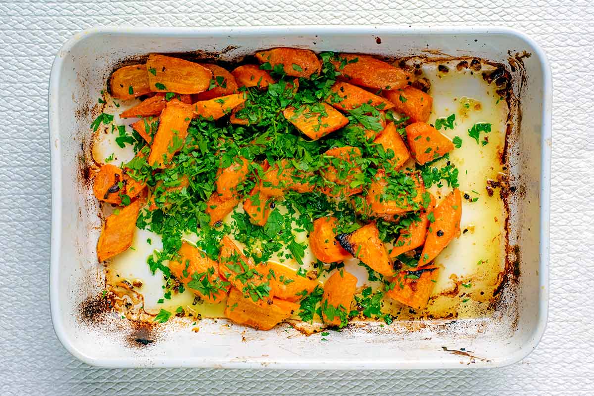 Cooked carrots in a baking dish with chopped parsley scattered over them.