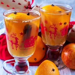 Christmas glasses containing Mulled Hot Apple Juice . An apple, cracker and red towel are in the background
