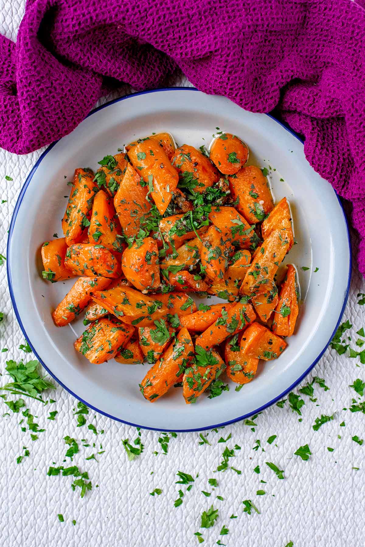 A white bowl full of roasted carrots, next to a purple towel.