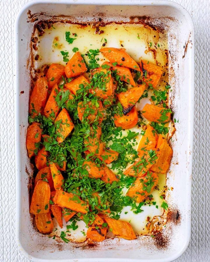 Cooked carrots in a baking dish with chopped parsley scattered over them.