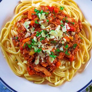 A white plate with mushroom bolognese and spaghetti.
