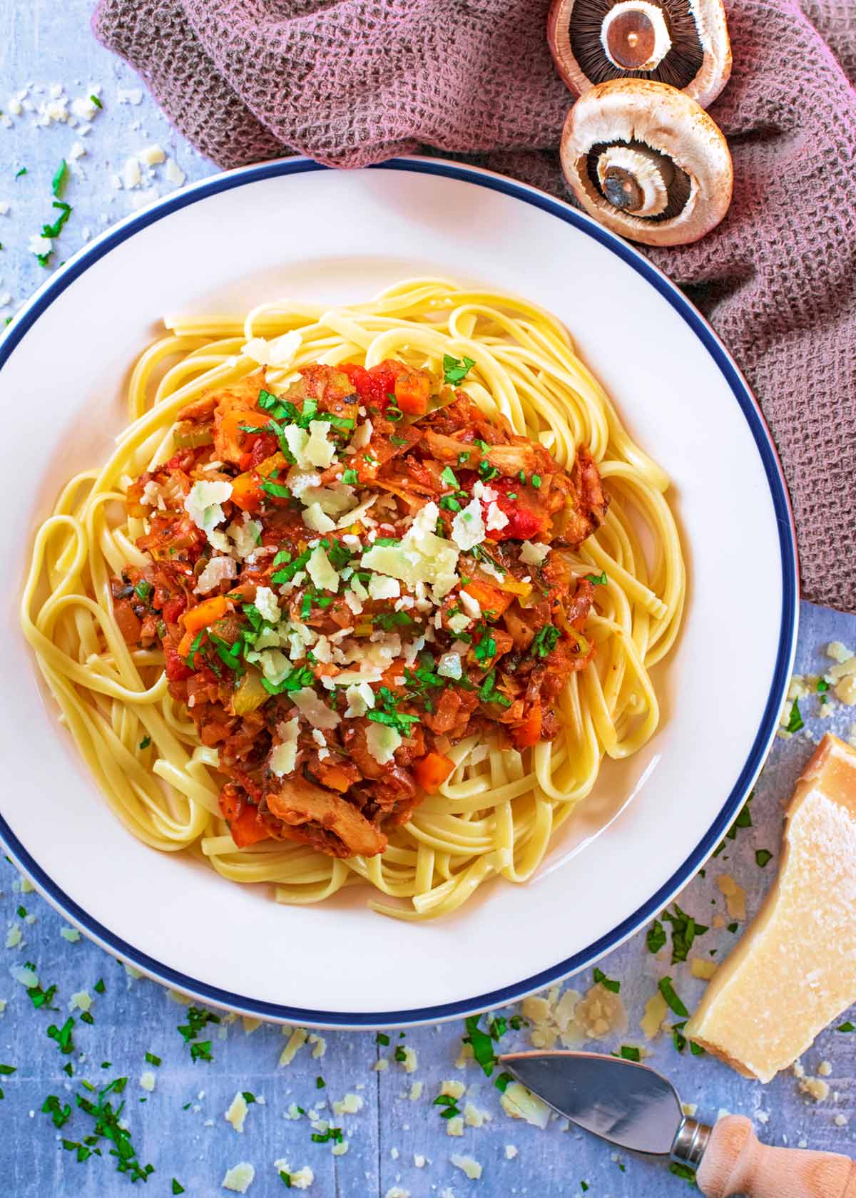 Bolognese and spaghetti on a white plate with a block of parmesan cheese next to it.