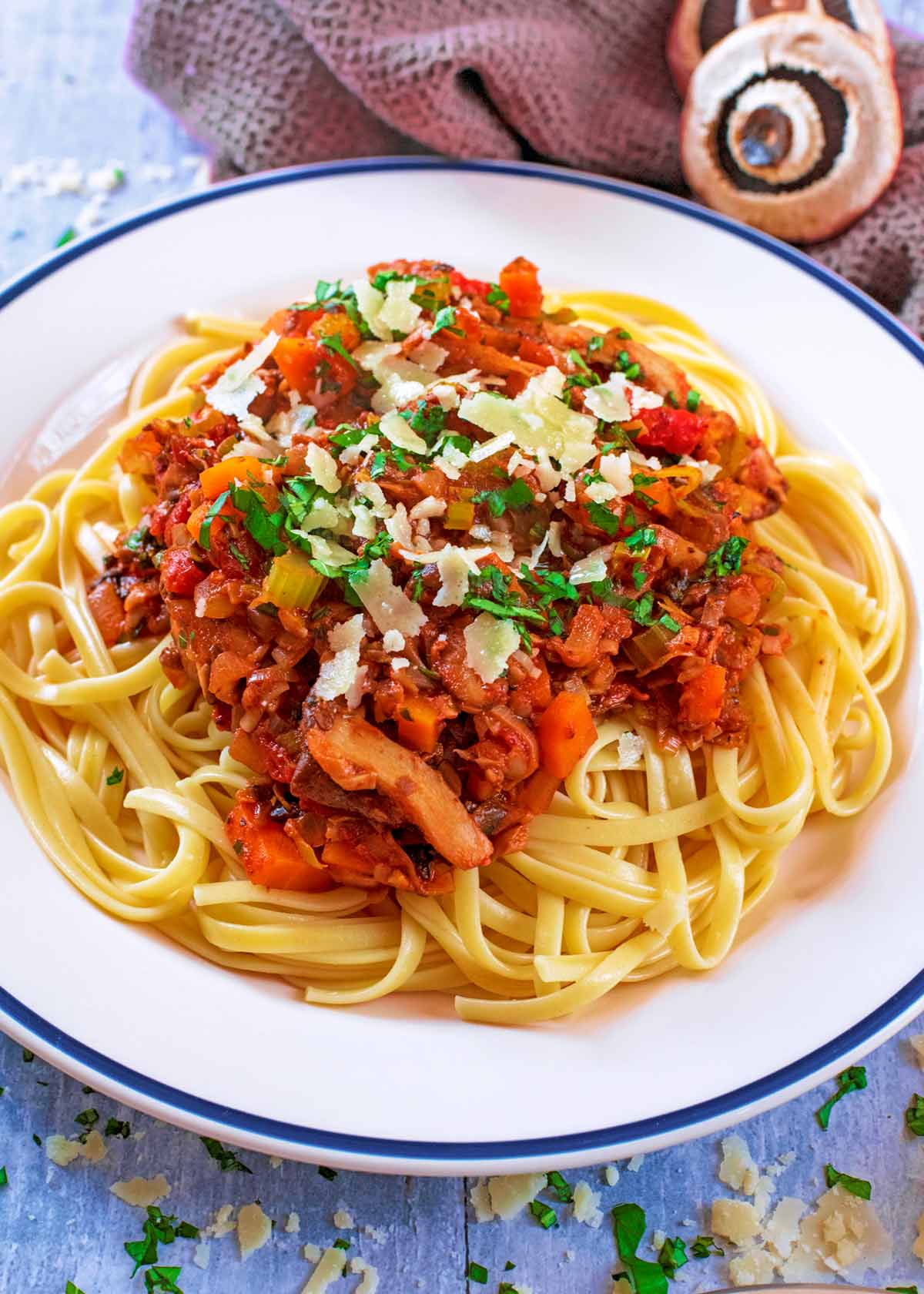 Pasta bolognese on a blue rimmed plate with parmesan and cheese knife.